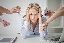 Stock photo of a woman stressed out by all her responsibilities. This is depicted by several hands holding out various tasks in front of her; two phone calls, a stack of paperwork, an upcoming deadline.