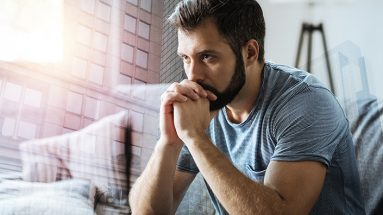 Stock photo of a man sitting in his city apartment, contemplating his day.