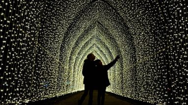 Stock photo of a silhouette of two people walking through a tunnel of christmas lights