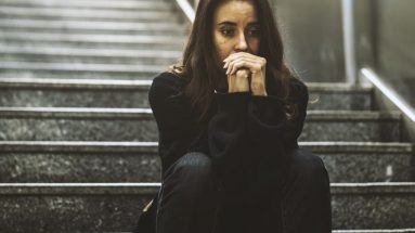 Stock photo of a woman sitting down on a set of stair covering her mouth in distress.