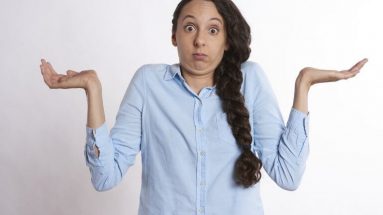 Stock image of a young brunette woman shrugging her shoulders & holding her hands up