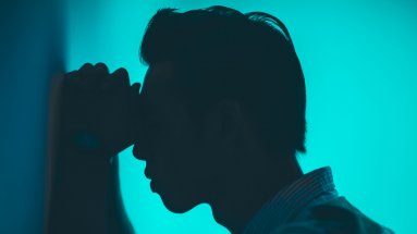 Stock photo of a man resting his head against his hands up against a wall