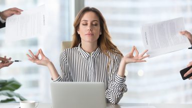 Stock image of a woman sitting in front of her computer staying calm while hands from other people are giving her things to do