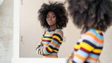 Stock photo of a Black woman looking into the mirror while wearing a colorful striped sweater