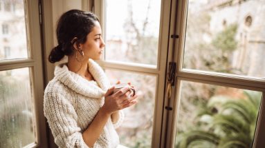 Stock photo of a sad woman at home staring out the window holding a mug