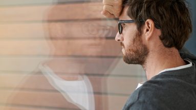 Stock photo of a young man leaning against a glass window looking pensive