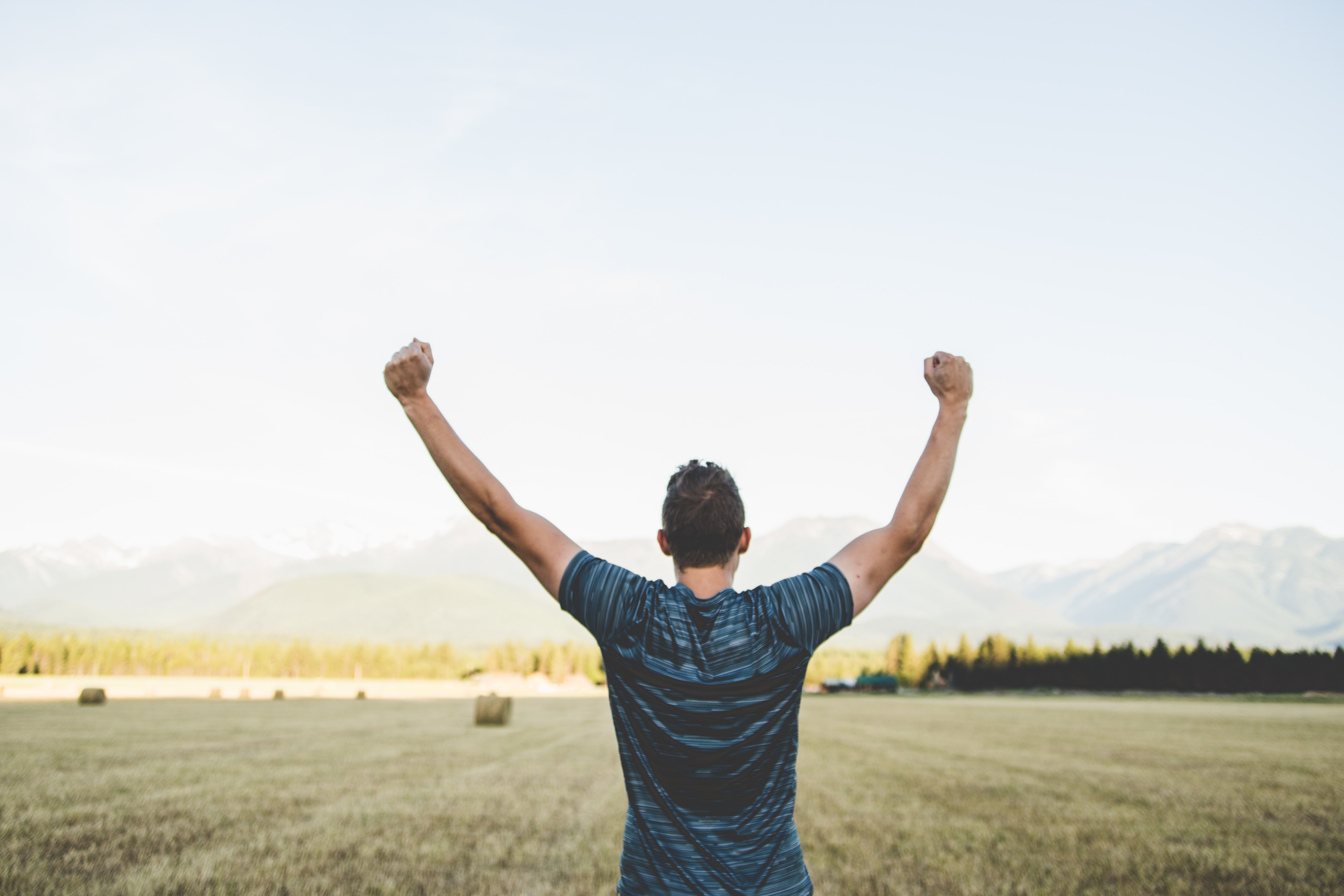 Stock photo of a man in a field with his hands raised over his head in a triumphant manner